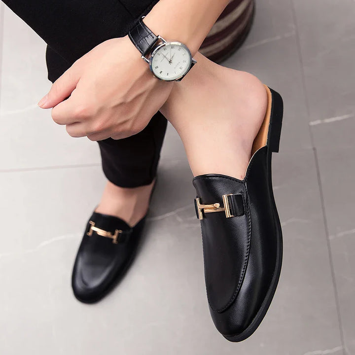 Santino Backless Slide Loafers in black with gold bit detail, styled with a watch, showcasing a sleek and polished look.
