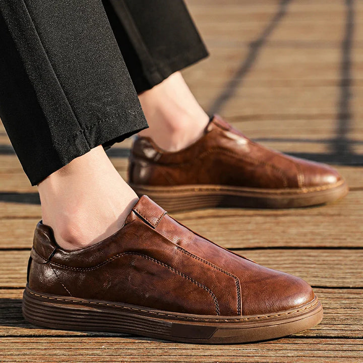 Brown genuine leather slip-on shoes on wooden surface, designed for comfort and everyday wear.