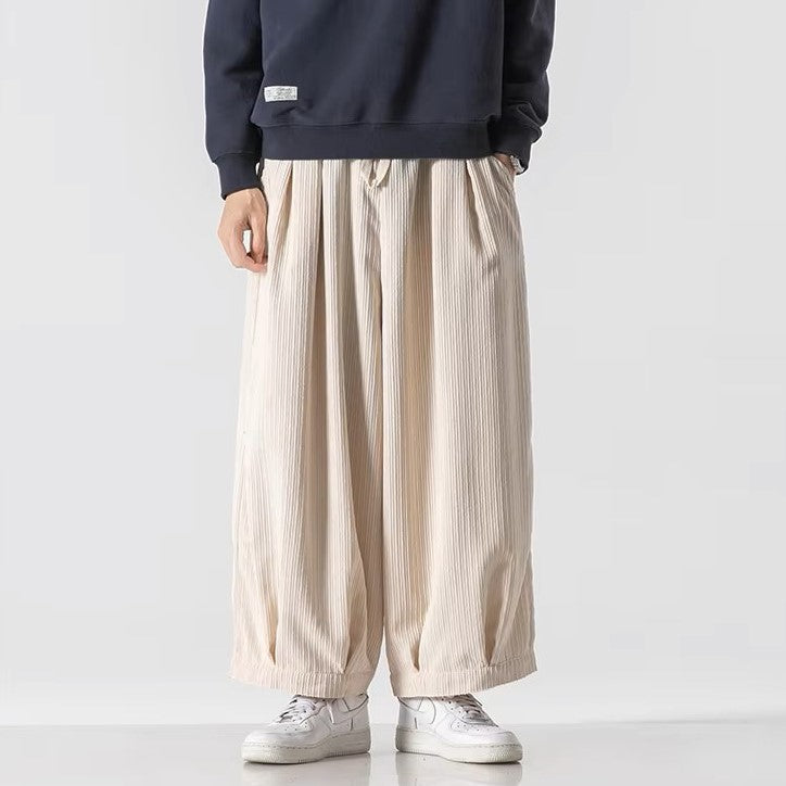 Oversized cream corduroy pants with deep pleats and elastic waistband, styled with a navy top and white sneakers.