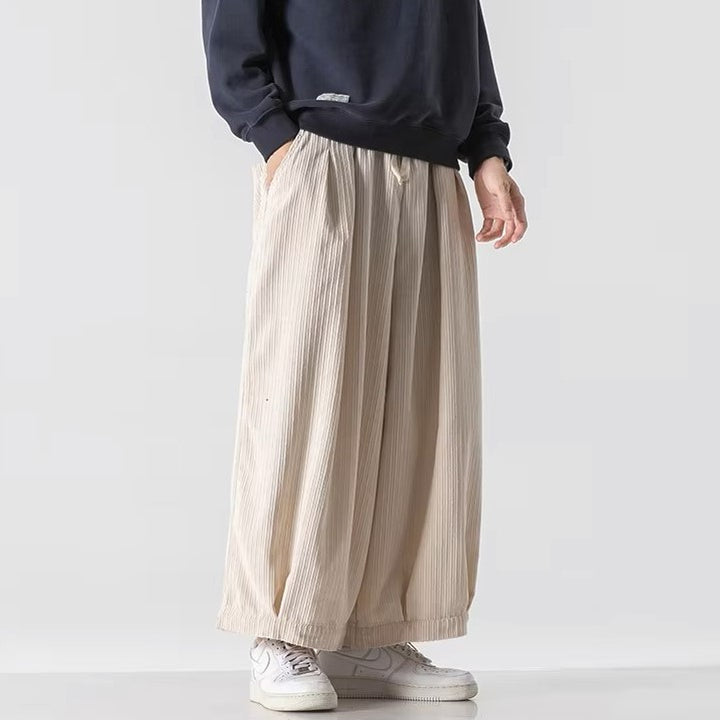 Oversized beige corduroy pants with deep pleats and elastic waistband for comfort and style.