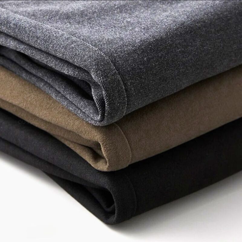Stack of folded Hudson Tailored Trousers in grey, brown, and black fabrics showcasing softness and quality.