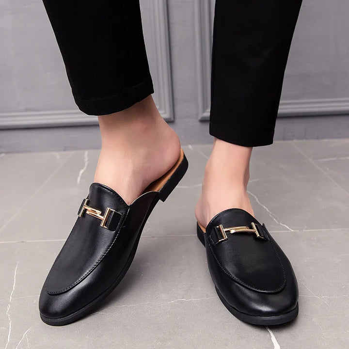 Santino Backless Slide Loafers in black with gold bit hardware, showcasing a sleek slip-on design on a person.