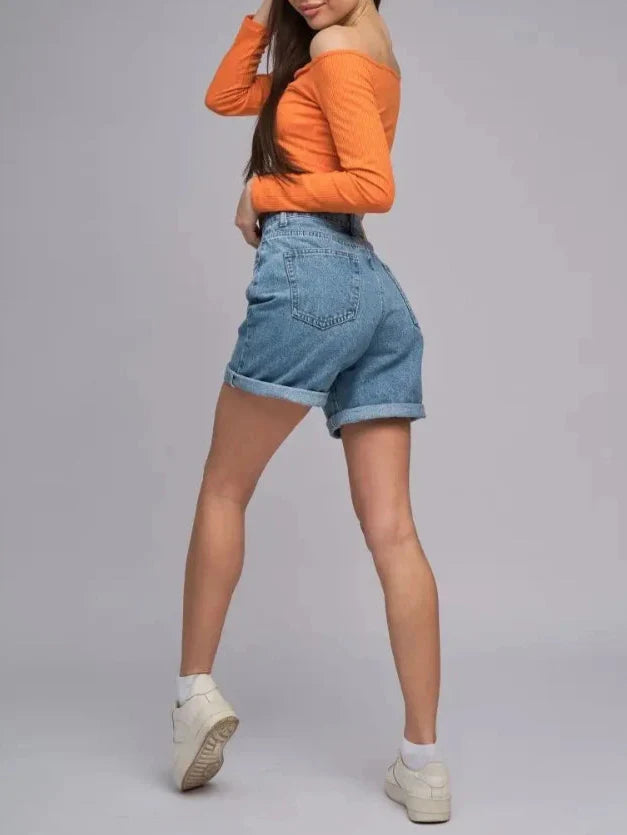 Model in orange top showcases Lyra Vintage High Waist Denim Shorts with rolled hems and structured fit.