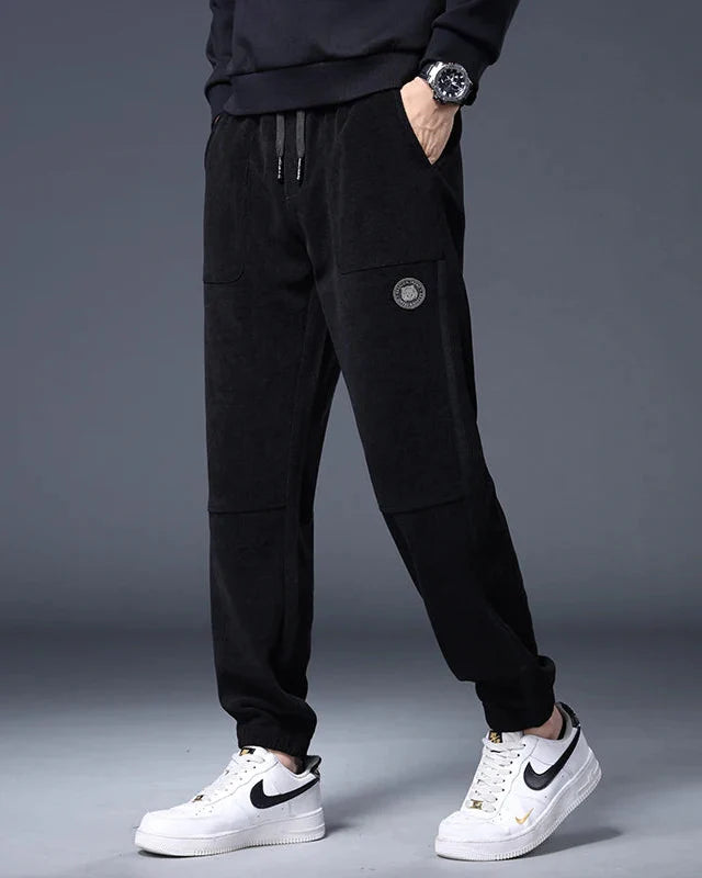 Black corduroy joggers with adjustable drawstring, large pockets, and clean ankle cuffs for a relaxed fit.