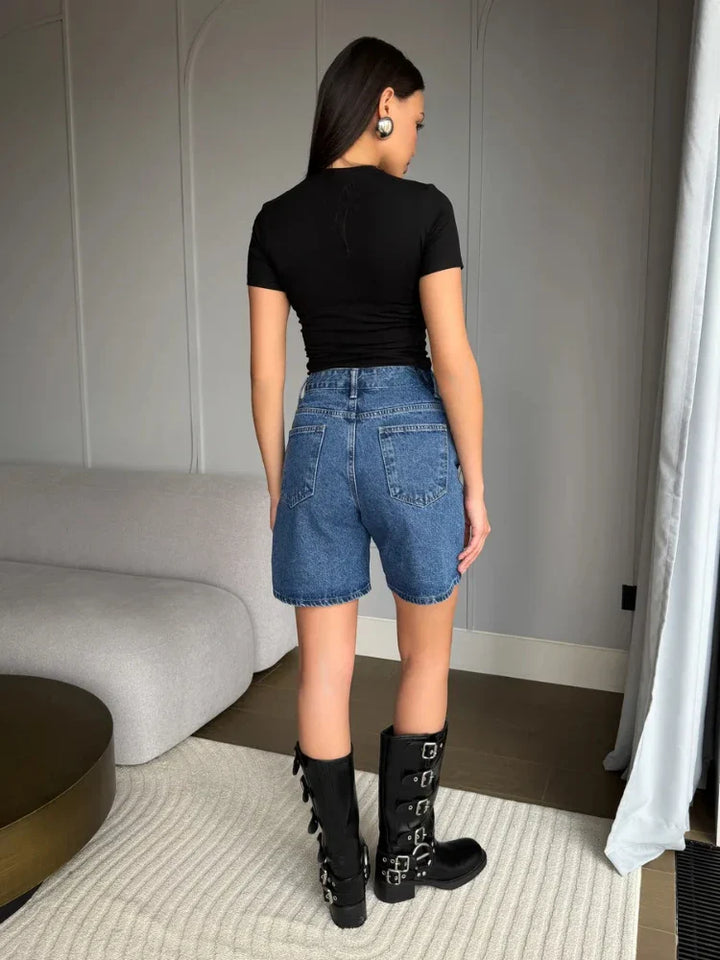 Back view of a model wearing Lyra vintage high waist denim shorts with a black fitted top and stylish knee-high boots.