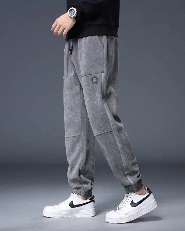 Gray corduroy joggers with adjustable drawstring waist and roomy pockets, styled with white sneakers.
