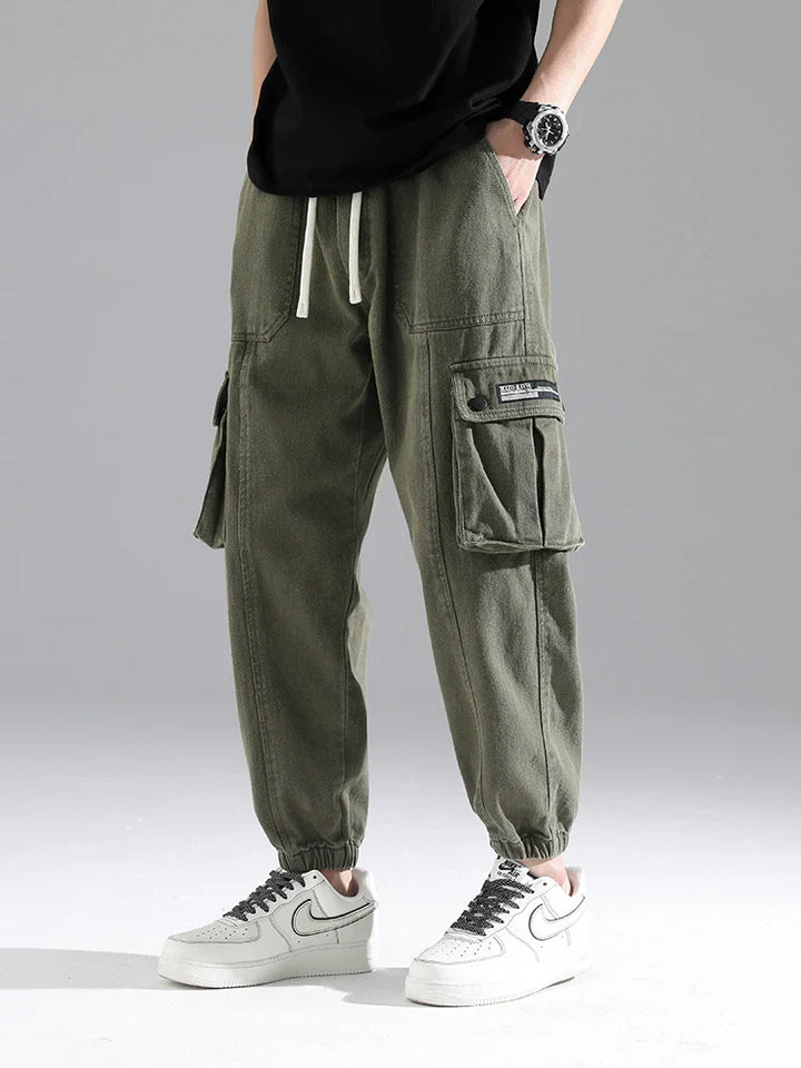 Lennox cargo joggers in heavyweight cotton blend with oversized snap pockets and elastic ankle cuffs, styled with casual sneakers.