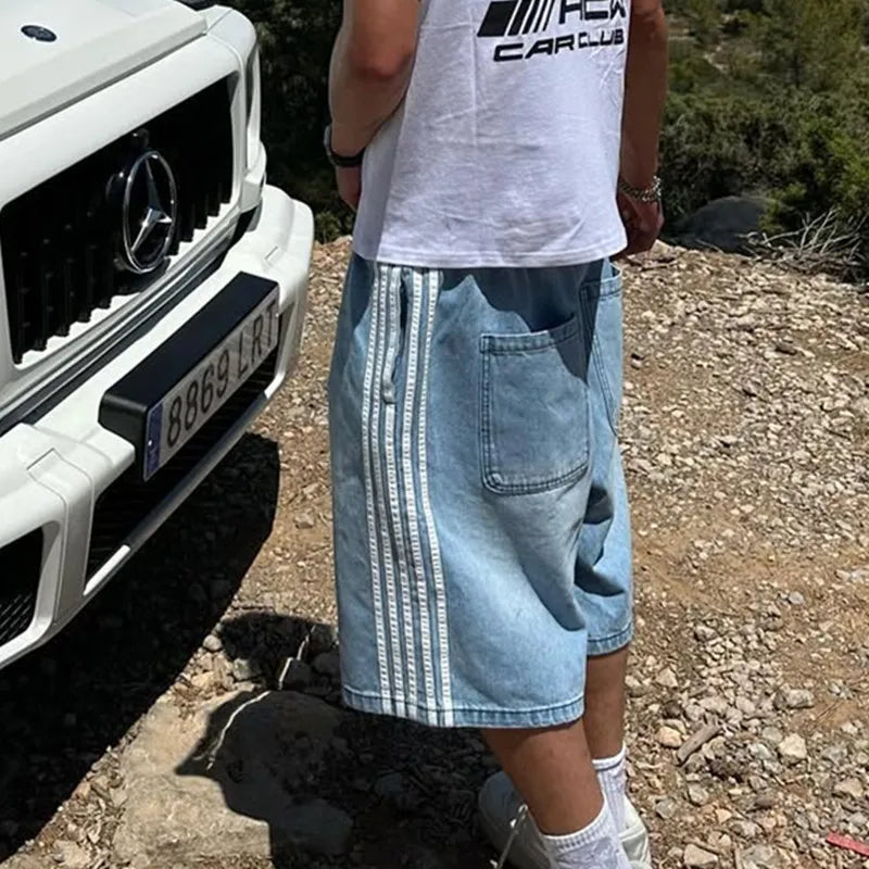 Person wearing Jax Denim Shorts with bold side stripes, relaxed fit, and washed finish, beside a luxury SUV.