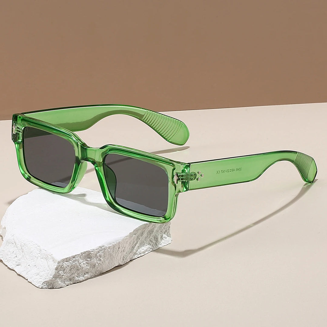 Green square-frame sunglasses with dark lenses and clear arms resting on a stone surface.