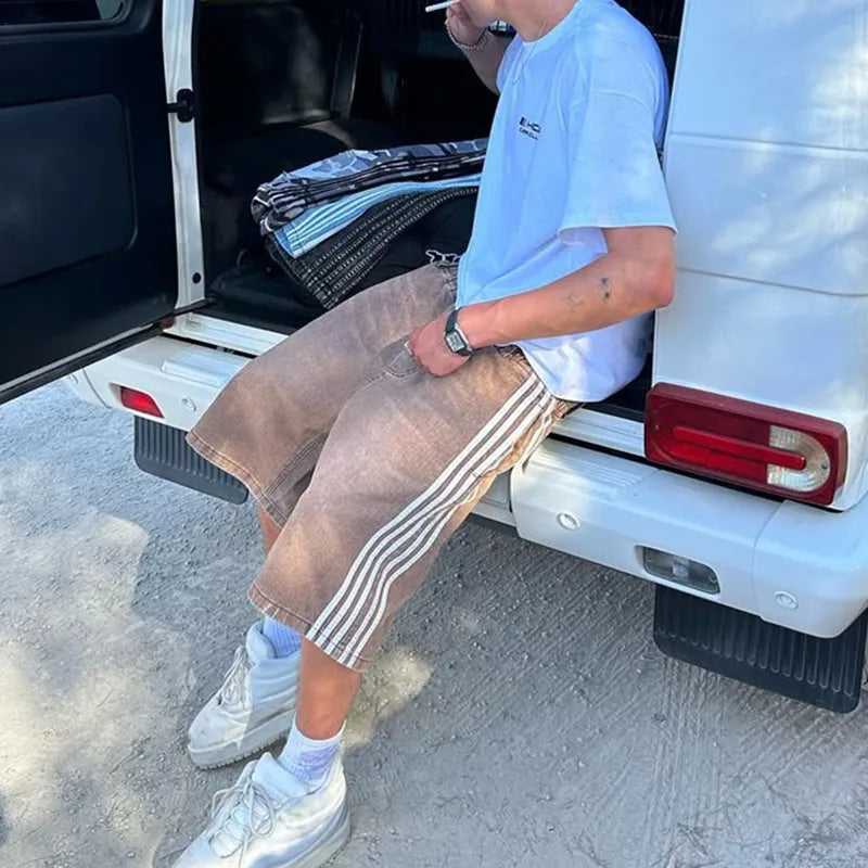 Model wearing Jax Denim Shorts with side stripes, relaxed fit, sitting by a vehicle, showcasing casual street style.