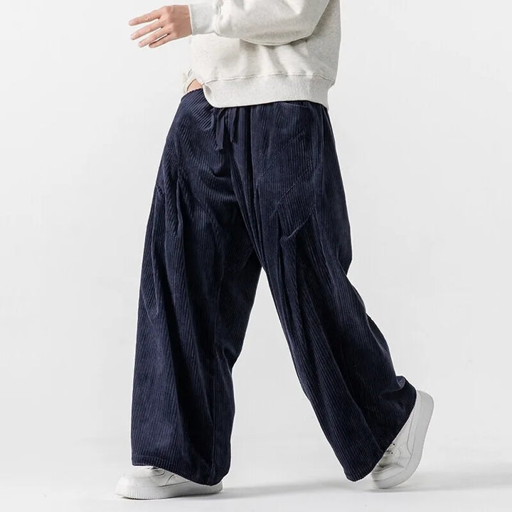 Model wearing wide-leg Hollis Corduroy Pants in navy, showcasing deep pleats and a smooth elastic waistband.