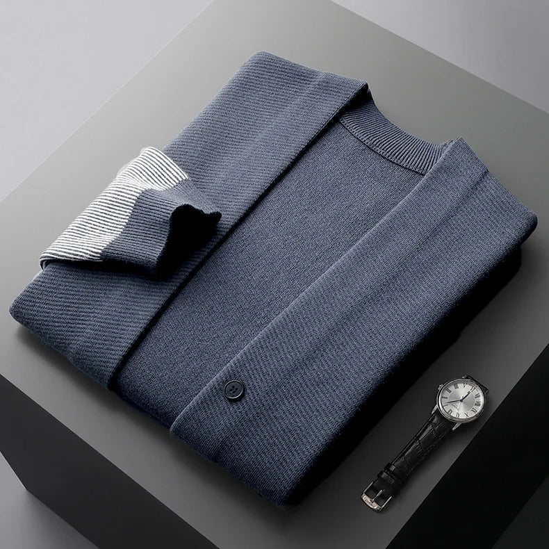 Rowan Merino cardigan in navy with ribbed contrast sleeves, neatly folded alongside a stylish watch on a gray surface.