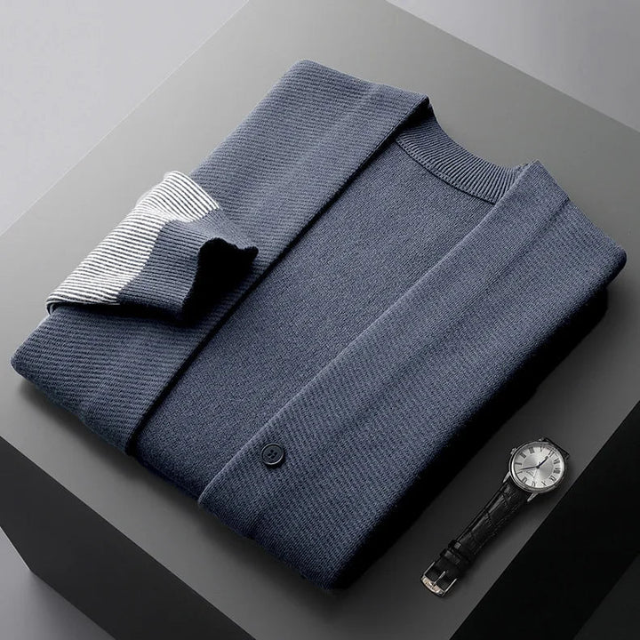 Rowan Merino cardigan in navy with ribbed contrast sleeves, neatly folded alongside a stylish watch on a gray surface.