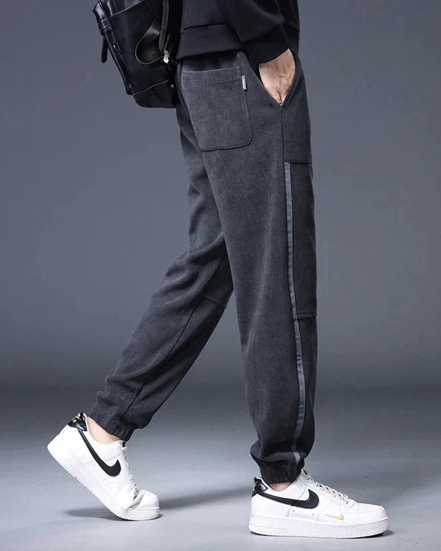 Amos Corduroy Joggers in dark gray, featuring a relaxed tapered fit, large pockets, and clean ankle cuffs.