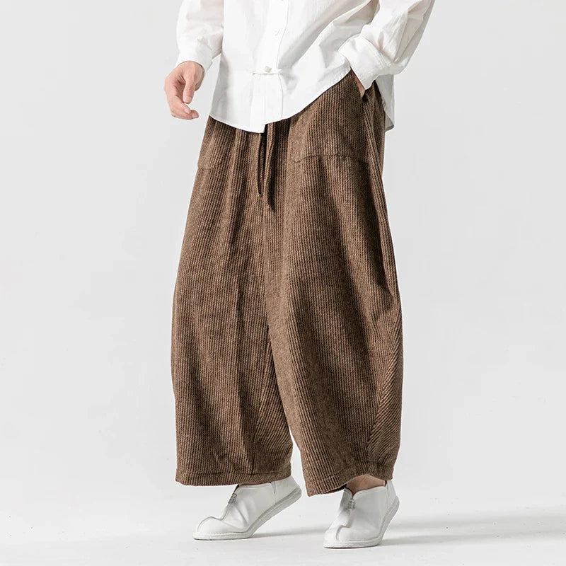 Henderson wide-leg corduroy pants in brown, featuring deep pleats and an elastic waistband for comfort and style.