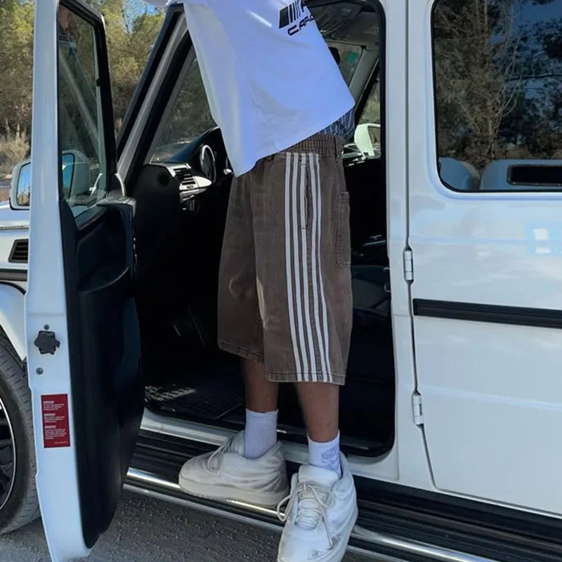 Model wearing Jax Denim Shorts in a vintage wash with bold side stripes, stepping out of a white vehicle.