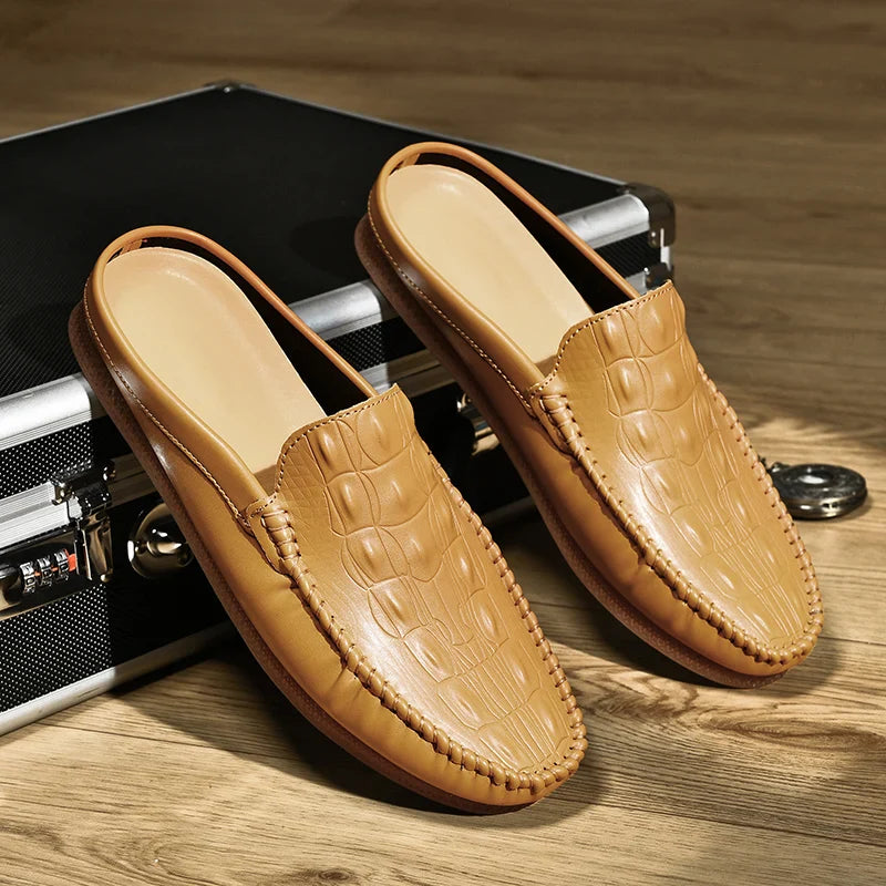 Gianni backless slide loafers with embossed upper and classic moc toe design on vintage suitcase.