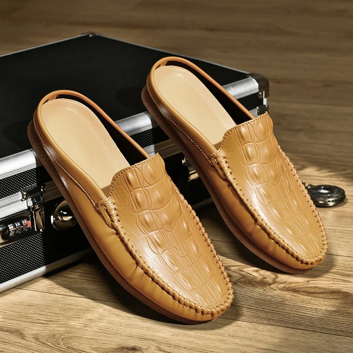 Gianni backless slide loafers with embossed upper and classic moc toe design on vintage suitcase.