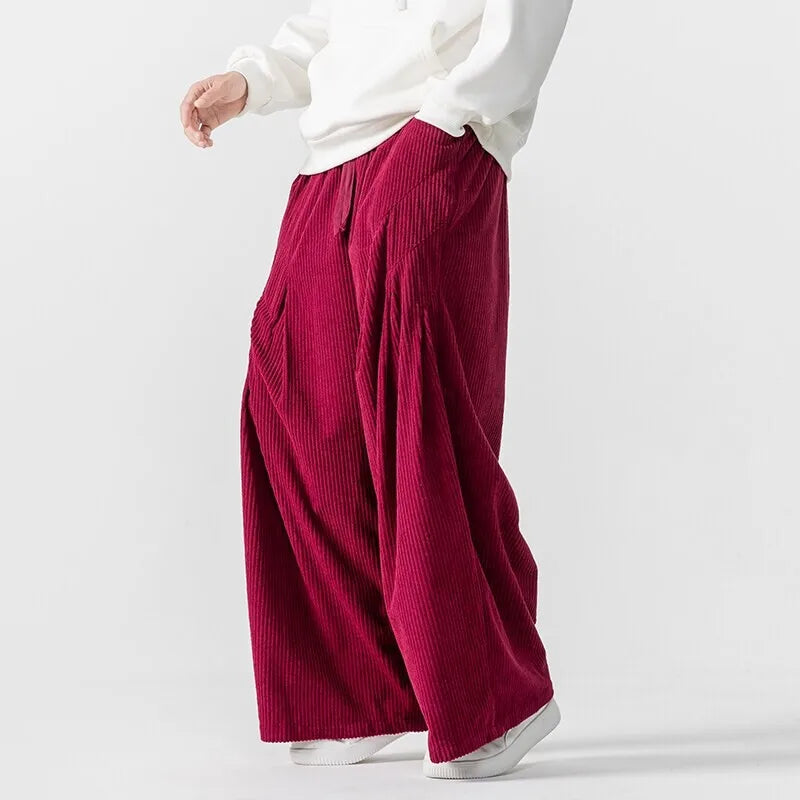 Side view of Hollis Corduroy Pants in rich burgundy with deep pleats and elastic waistband, showcasing wide-leg silhouette.