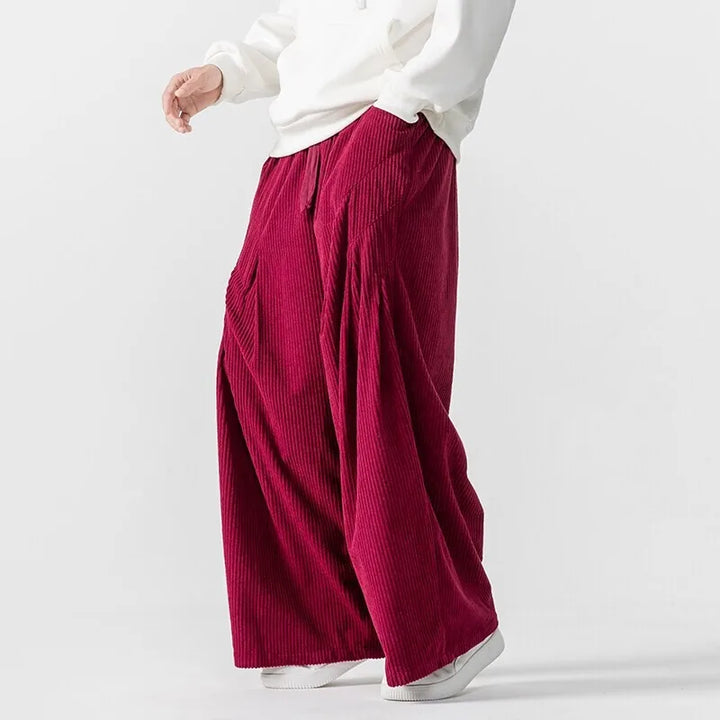 Side view of Hollis Corduroy Pants in rich burgundy with deep pleats and elastic waistband, showcasing wide-leg silhouette.