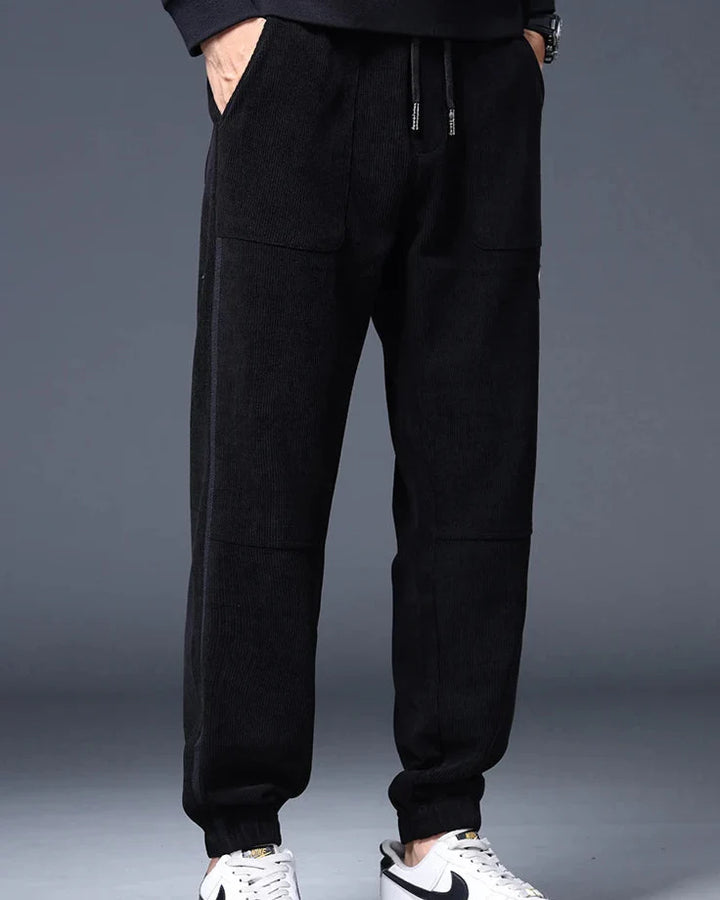 Men's black wide-wale corduroy joggers with relaxed tapered fit, functional pockets, and adjustable drawstring waist.