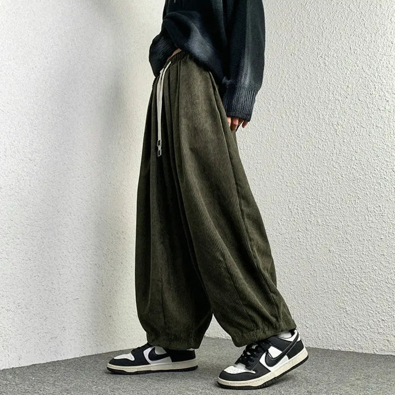 Relaxed fit Arlo corduroy pants in dark green with wide legs and adjustable drawstring waist, styled with sneakers.