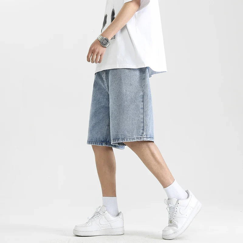 Stylish man in relaxed denim shorts paired with a graphic tee and white sneakers, showcasing a skater-inspired look.
