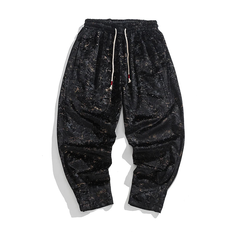 Black crushed velvet joggers with elastic cuffs and drawstring waist, showcasing a relaxed fit and textured finish.