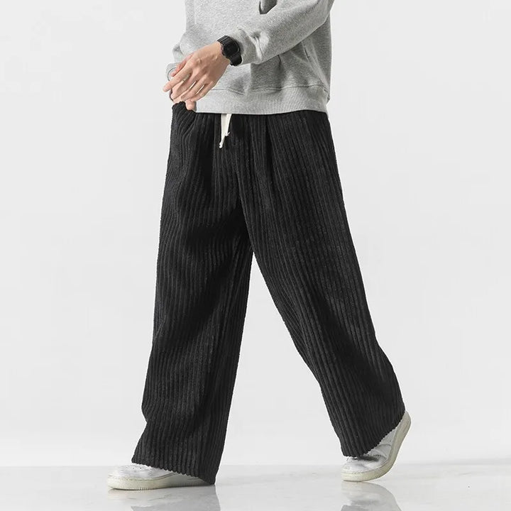 Casual model wearing black corduroy pants with elastic waistband and wide-leg fit, showcasing retro style.