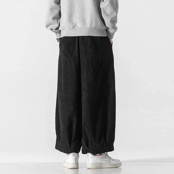 Back view of black oversized corduroy pants featuring deep pleats and a relaxed fit, paired with a gray sweatshirt.