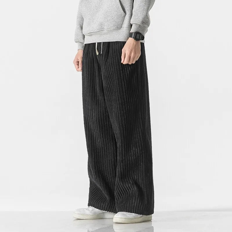 Black corduroy pants with wide-leg fit, elastic waistband, and adjustable drawstring, styled with a gray sweatshirt.
