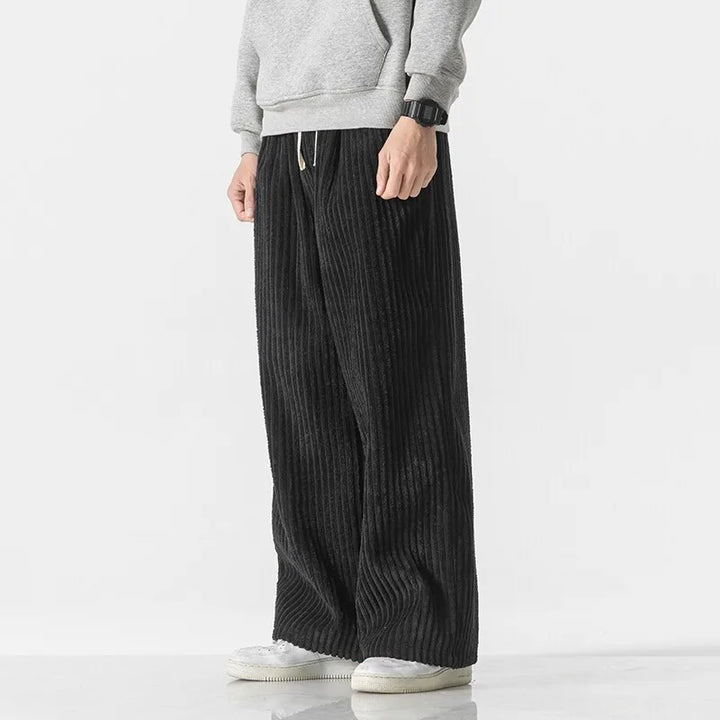 Black corduroy pants with wide-leg fit, elastic waistband, and adjustable drawstring, styled with a gray sweatshirt.