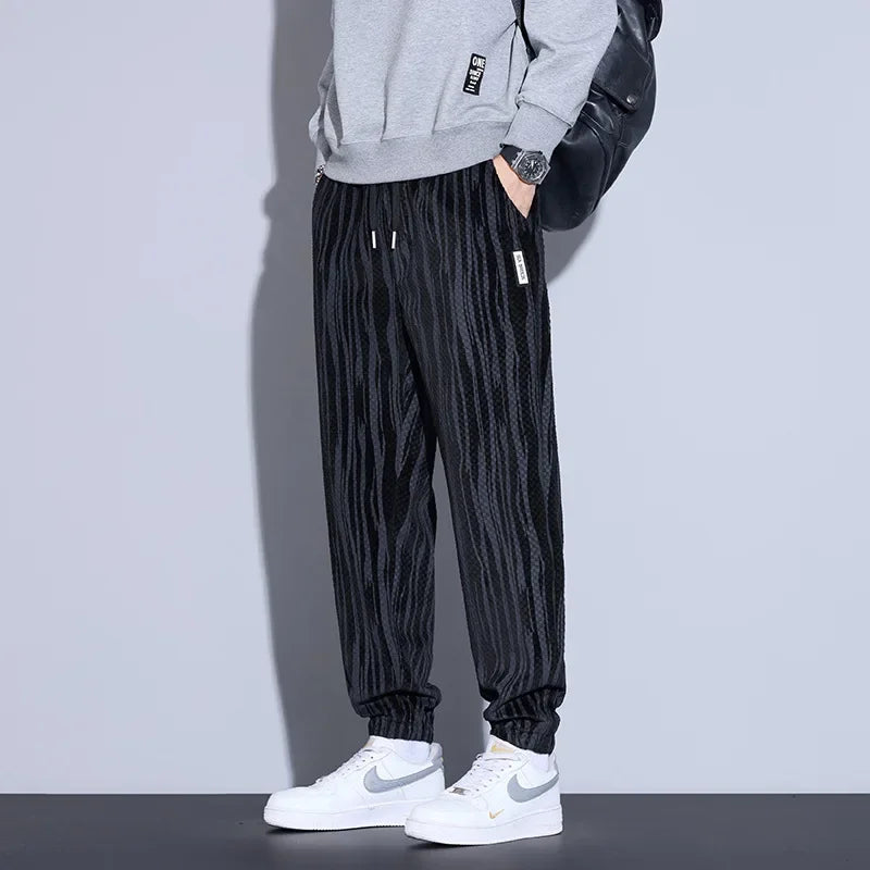 Men's black checkered corduroy pants paired with a gray sweatshirt and white sneakers, showcasing a trendy casual look.