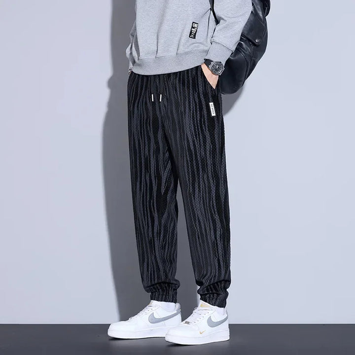 Men's black checkered corduroy pants paired with a gray sweatshirt and white sneakers, showcasing a trendy casual look.