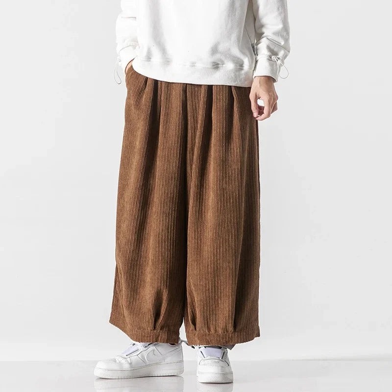 Oversized brown corduroy pants with deep pleats and relaxed fit, worn with a white sweatshirt and sneakers.