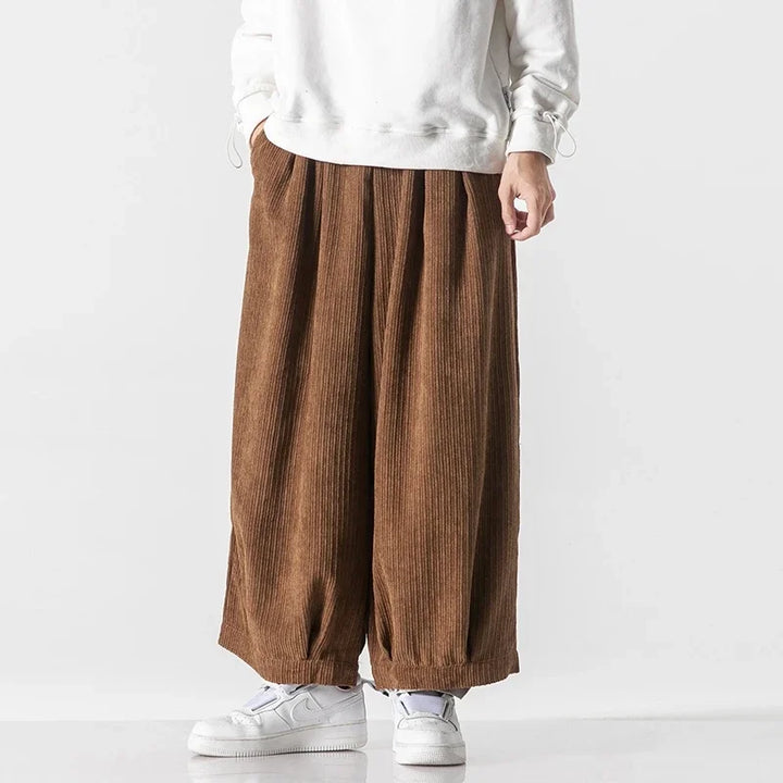 Oversized brown corduroy pants with deep pleats and relaxed fit, worn with a white sweatshirt and sneakers.