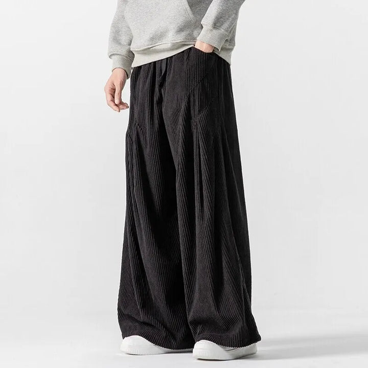 Hollis Corduroy Pants in black, featuring wide-leg design, smooth elastic waistband, and deep pleats for a bold silhouette.