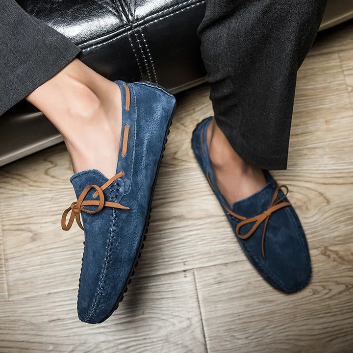 Monte Carlo suede loafers in blue on a wooden floor, featuring premium leather laces and hand-stitched details.